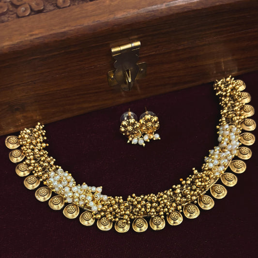 Gold temple jewellery set with pearls, featuring intricate designs and matching earrings, displayed on velvet.