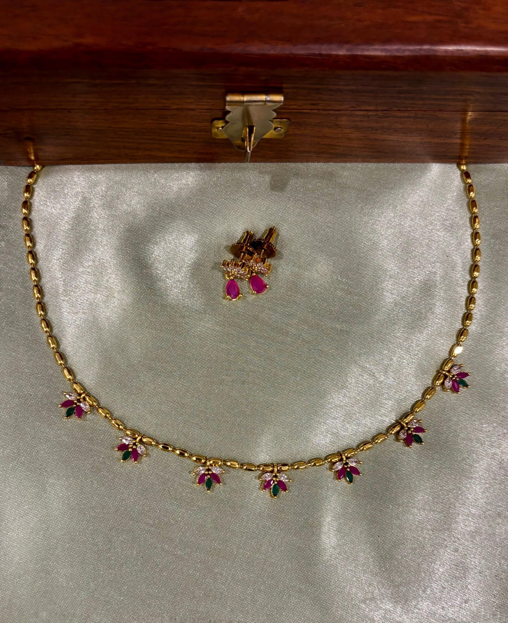 Gold necklace with floral gemstone accents and matching earrings on satin fabric
