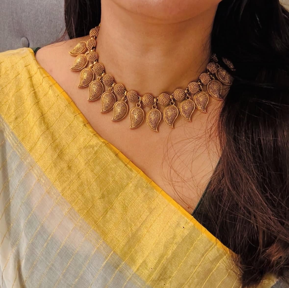 Elegant South Indian gold temple necklace with intricate leaf motifs, paired with a yellow saree.