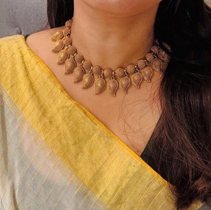 Elegant South Indian gold temple necklace with intricate leaf motifs, paired with a yellow saree.