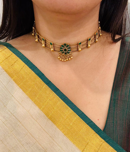 Gold choker necklace with green gemstones, worn with traditional saree, South Indian bridal jewelry